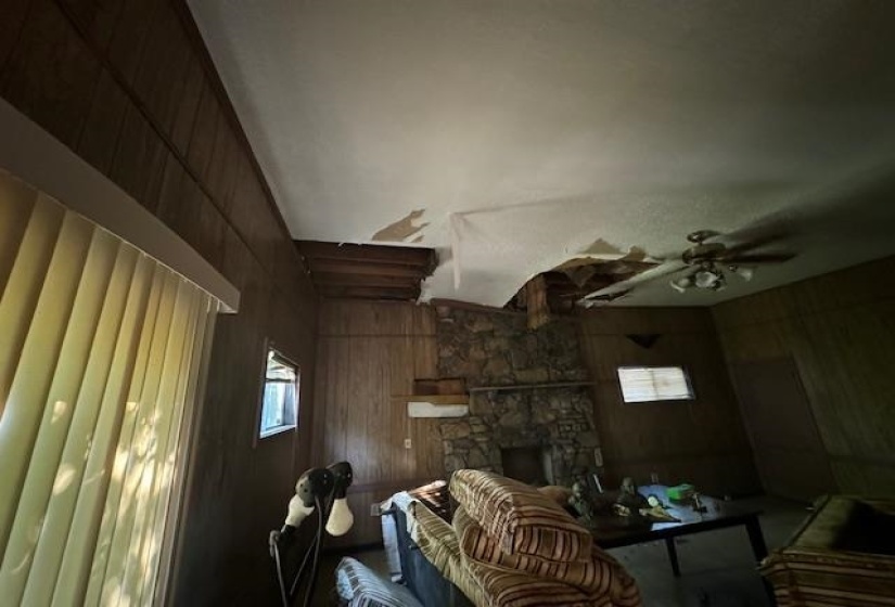 Interior space featuring wood paneling walls, a stone-clad fireplace, and a ceiling fan