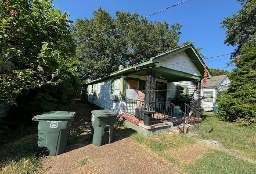 Single-story residence featuring white siding, a green-trimmed gable roof, and an inviting front porch with decorative wrought iron columns and railings