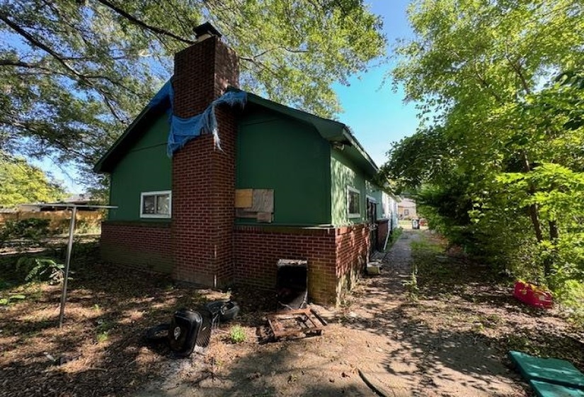 Exterior featuring a brick chimney, green siding, and a partial brick foundation