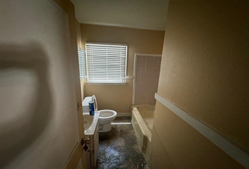 Bathroom with a single vanity, a toilet, and a bathtub with tiled walls