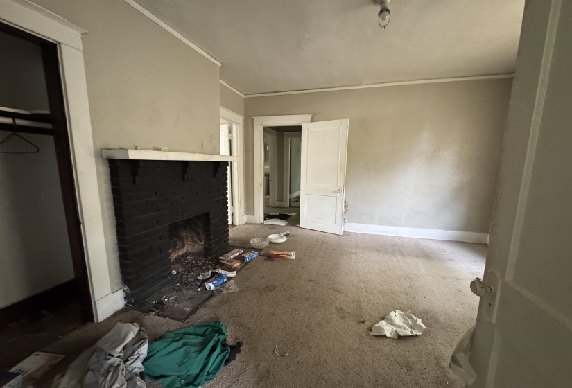 Room featuring a fireplace with a painted black brick surround and white mantel, light-colored walls, and a ceiling-mounted light fixture