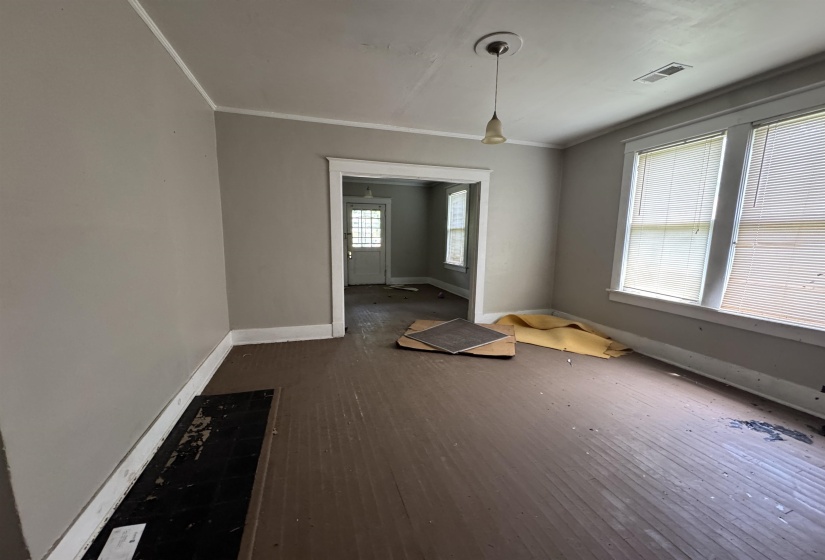 Interior room with painted wood-finish flooring, two large windows, a single pendant light fixture, and crown molding
