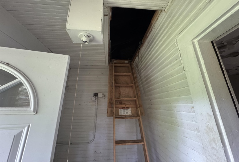 Pull-down attic access ladder with wood treads, positioned under a wood-paneled ceiling