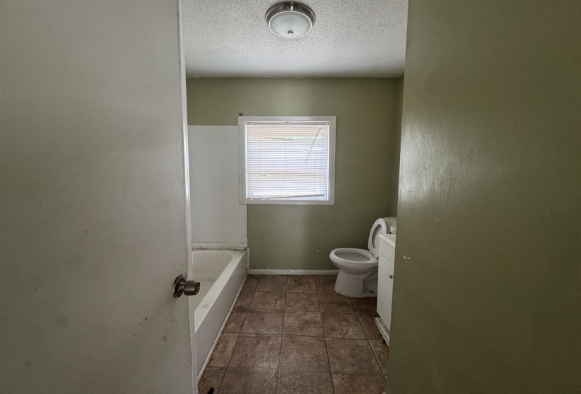 Bathroom featuring a tiled floor, window with horizontal blinds, built-in bathtub, and a white toilet