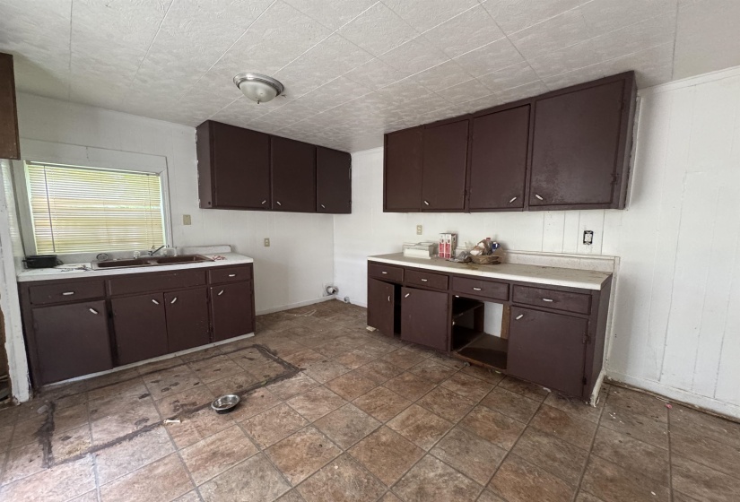 Kitchen space featuring upper and lower cabinetry with integrated hardware, a double basin sink, and a window with horizontal blinds