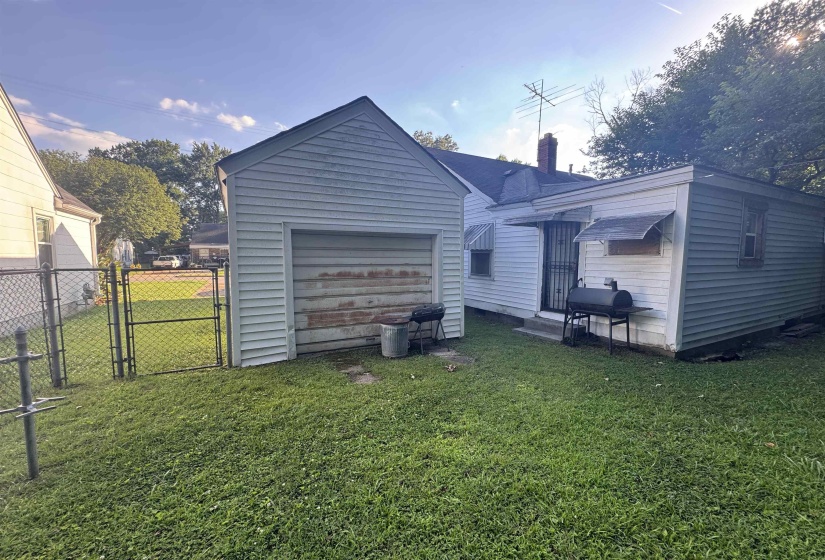 Detached garage with a roll-up door, chain-link fencing, and a separate structure featuring a side entrance