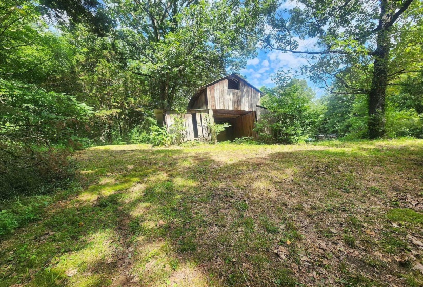 Barn structure with natural wood siding, surrounded by mature trees and a grassy clearing