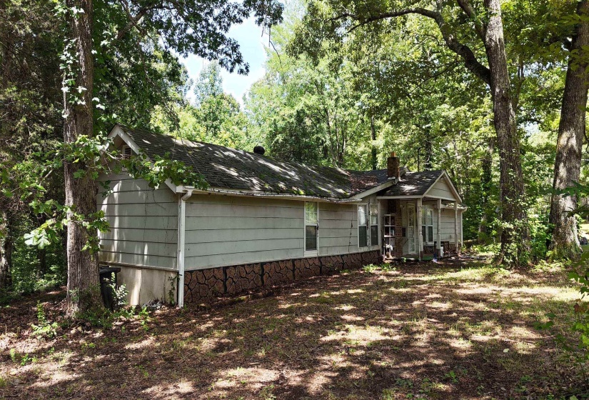 Ranch-style residence featuring a covered front porch with columns, a prominent brick chimney, and mature trees providing shade