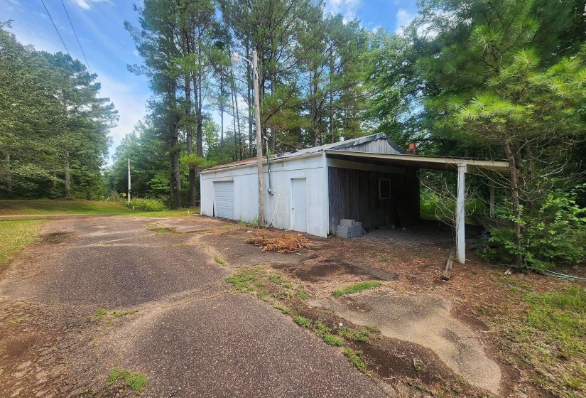Utility building featuring a single garage door, an attached carport, and a separate entry door