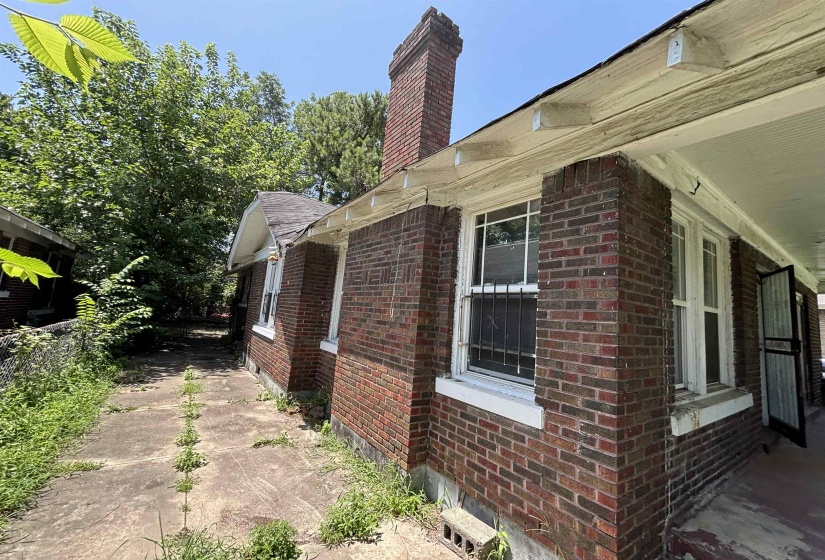 Brick exterior with a prominent brick chimney, multiple double-hung windows, and a covered porch area