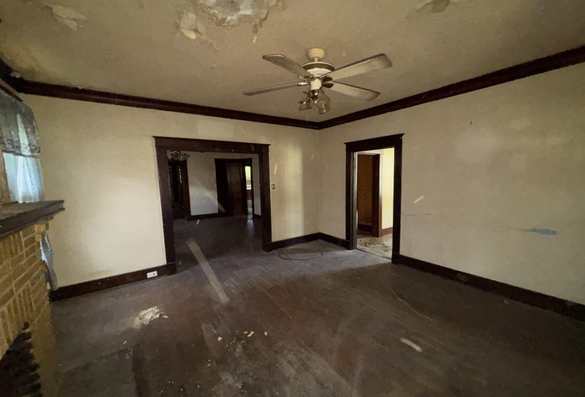 Hardwood flooring throughout, ceiling fan with light fixture, brick fireplace with mantel, dark wood trim, and multiple doorways