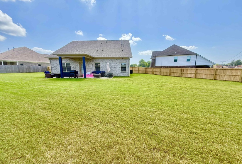 Expansive green lawn with a covered patio, featuring a light brick exterior and a privacy fence