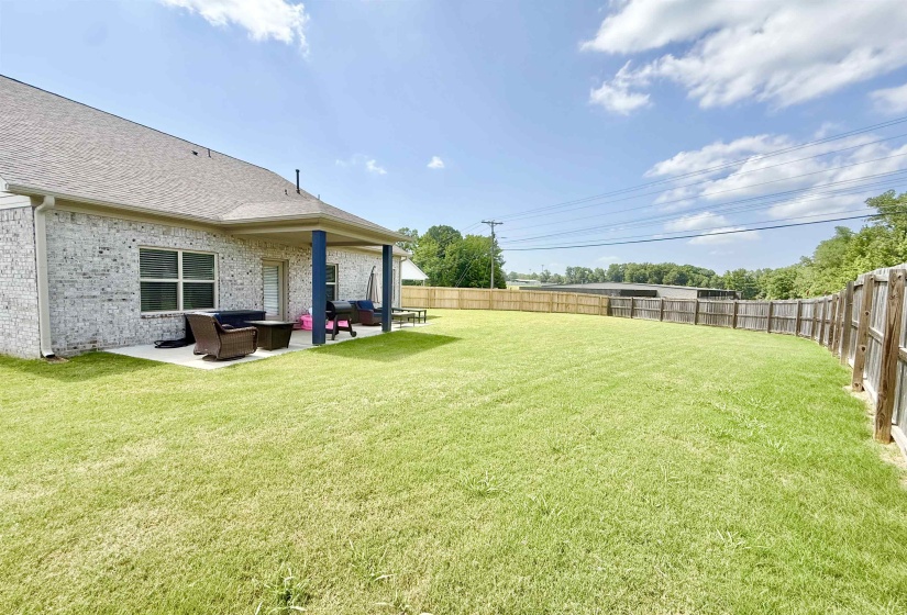 Spacious backyard featuring a manicured lawn, full wood fencing, and a covered patio with blue support columns