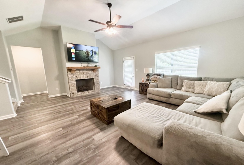 Living area featuring vaulted ceilings with a ceiling fan, wood-finish flooring, and a fireplace with a stone surround and wood mantel