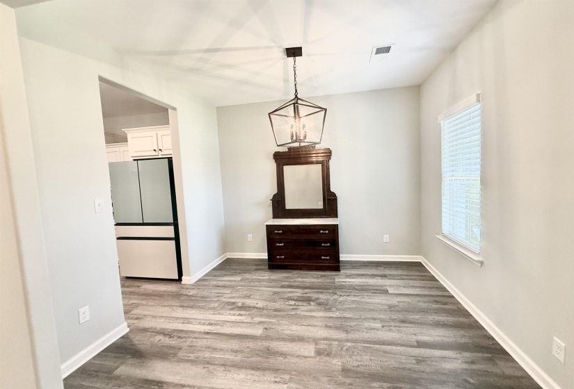 Open concept dining area featuring wood-finish flooring, a contemporary ceiling light fixture, and a window with blinds