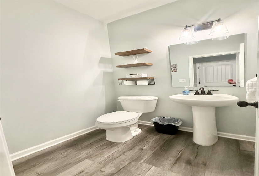 Powder room featuring wood-finish flooring, a white pedestal sink, and a matching white toilet
