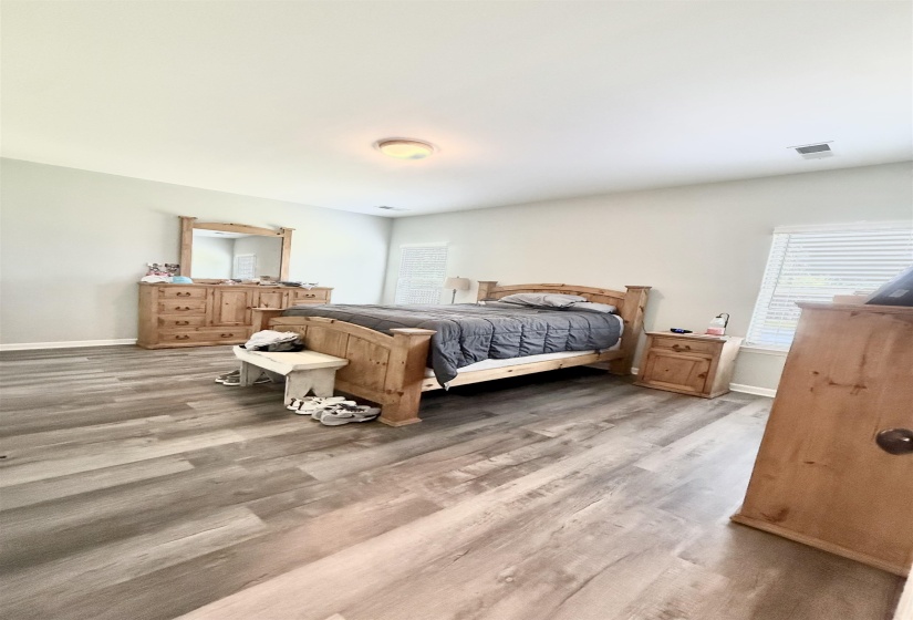 Spacious room featuring wood-finish flooring, a ceiling-mounted light fixture, white walls, and horizontal blinds on the window