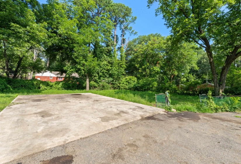 Concrete pad with surrounding green space, mature trees, and a paved area