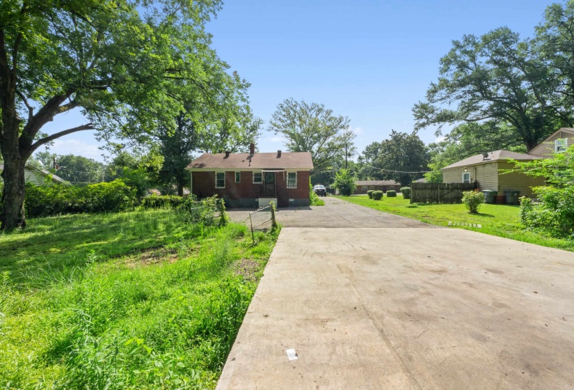 Expansive paved driveway leading to a brick exterior home with a gabled roof