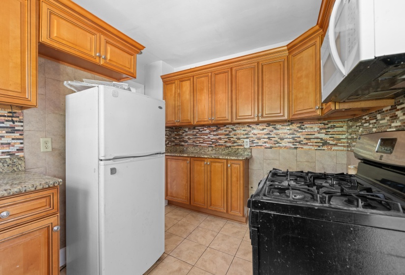 Kitchen featuring wood cabinetry, stone countertops, a tile backsplash, and tile flooring