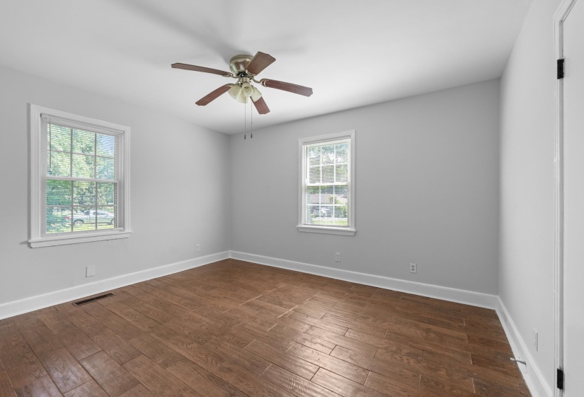 Room featuring wood-finish flooring, two windows with white trim, a ceiling fan with light fixture, and light gray painted walls
