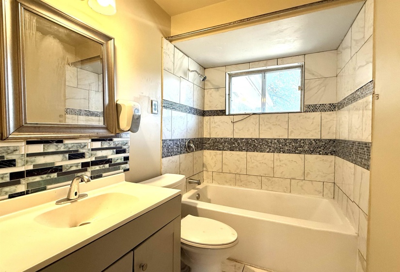 Bathroom featuring a combination bathtub and shower with white tile surround and decorative mosaic accents