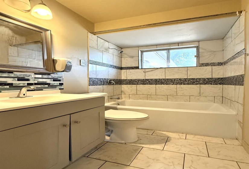 Bathroom featuring a tiled tub/shower combination with mosaic accents, a built-in window, and a vanity with an integrated sink and base cabinetry