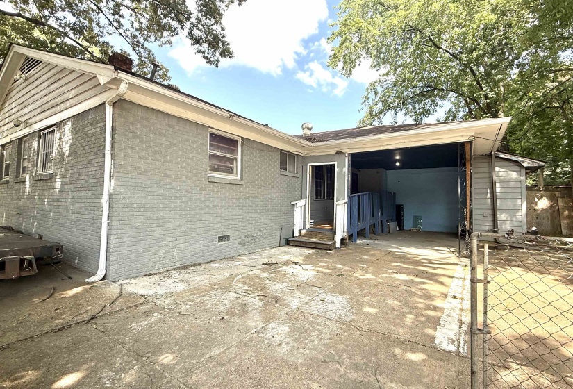 Rear exterior featuring painted brick siding, a covered carport, and a chain-link fence