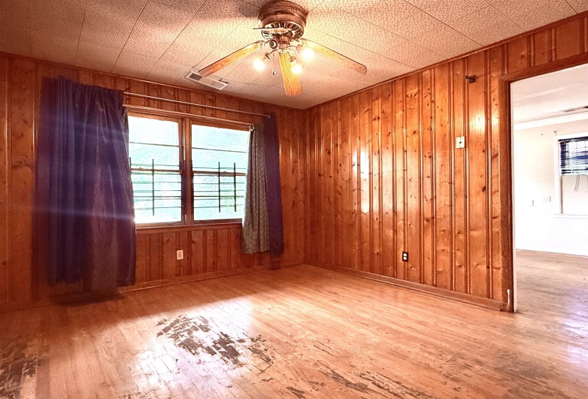 Room featuring wood paneling on walls, wood-finish flooring, and a ceiling fan with integrated lighting