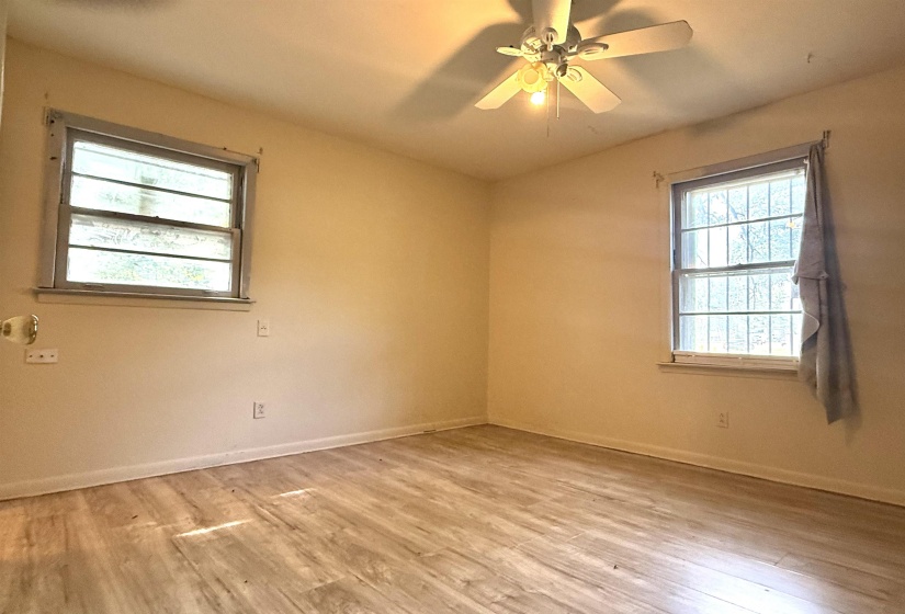 Room featuring wood-finish flooring, two windows with security bars, a ceiling fan with light fixture, and neutral-toned walls