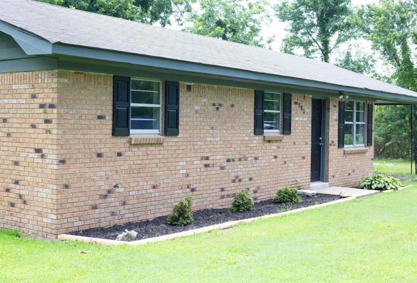 Brick exterior with dark shutters, a dark front door, and a covered entry