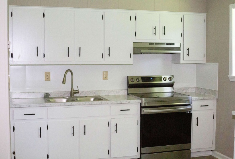 Kitchen featuring white cabinetry with black hardware, stainless steel sink with gooseneck faucet, light-toned countertops, and a modern stainless steel range with overhead ventilation