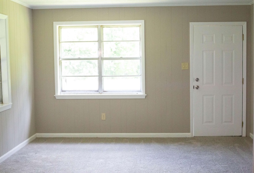 Carpeted room featuring a multi-pane window, paneled walls, and a paneled entry door