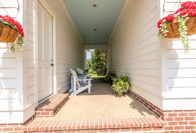Covered outdoor corridor featuring white siding, a blue ceiling, and a brick foundation