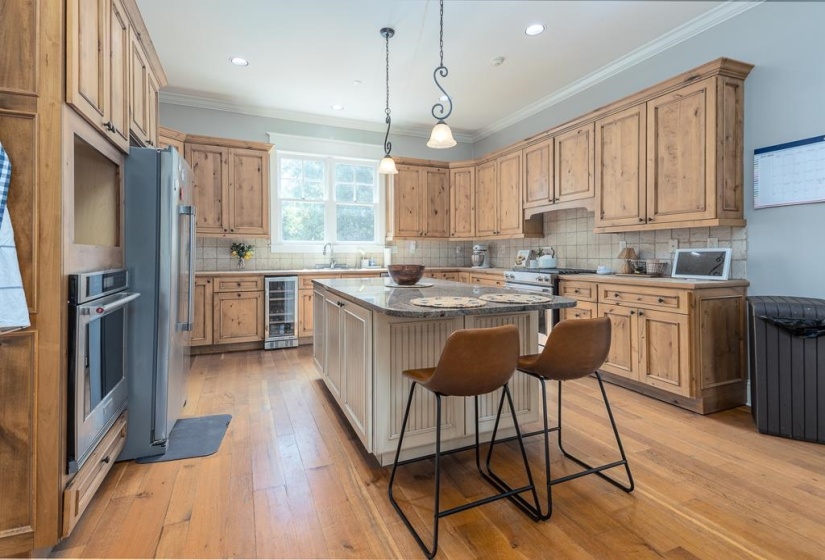 Spacious kitchen featuring extensive wood cabinetry, wood-finish flooring, a central island with a stone countertop, stainless steel appliances, and a built-in wine refrigerator