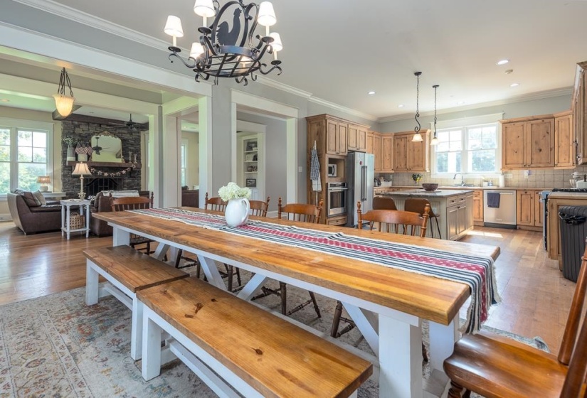 Spacious dining area with a long wood-finish table and benches, featuring an overhead decorative chandelier