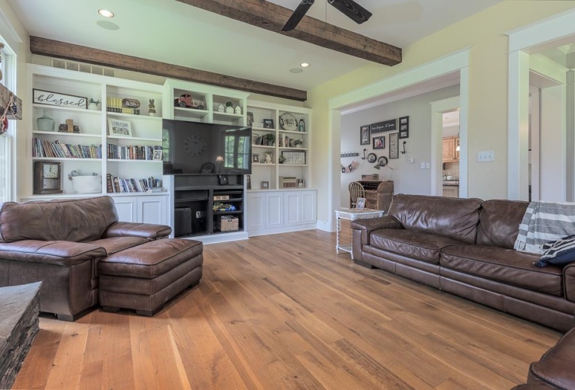 Living area featuring wood-finish flooring, exposed ceiling beams, built-in shelving, recessed lighting, and a ceiling fan