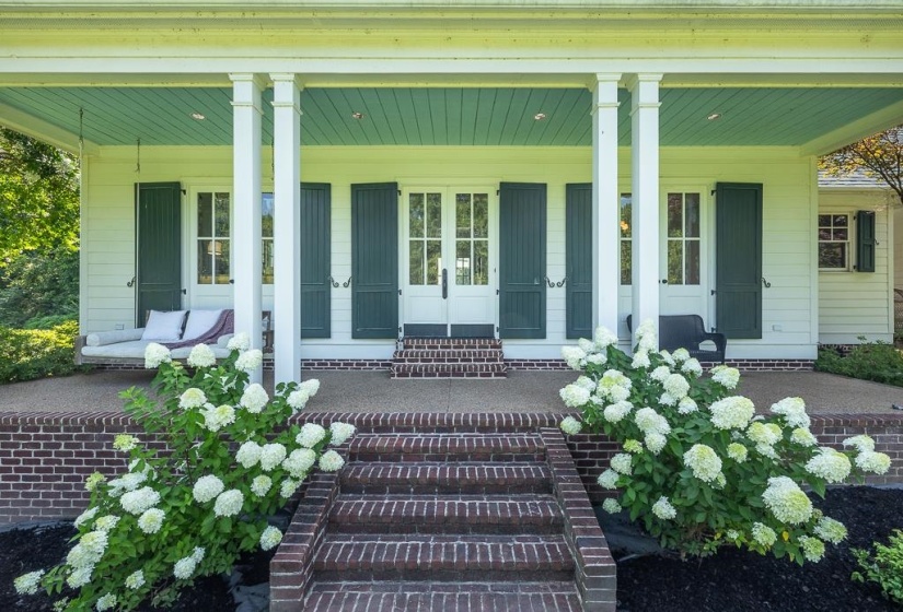 Front porch entry featuring brick steps, a brick foundation, four white columns, a light teal porch ceiling, and white blooming hydrangeas