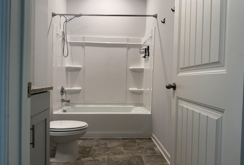Full bathroom featuring a white tub and shower combination with an integrated multi-shelf unit, a contemporary toilet, and stone-look flooring