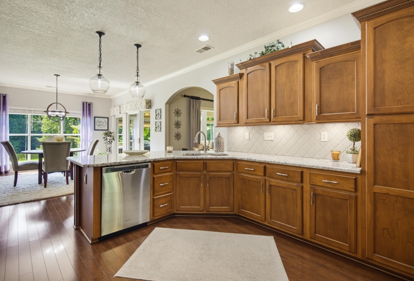 Gourmet kitchen featuring wood-finish flooring, custom cabinetry, stainless steel appliances, granite countertops, and a full tile backsplash