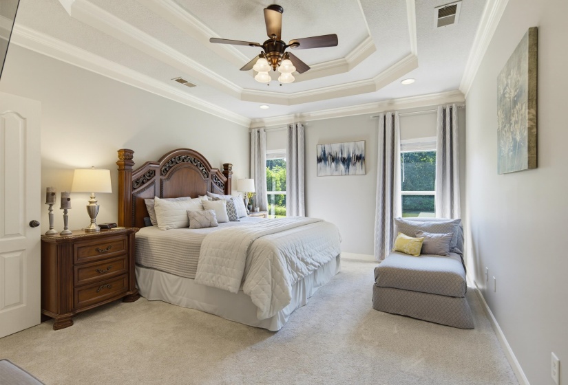 Spacious room featuring a tiered tray ceiling with crown molding, a ceiling fan with integrated lighting, light grey walls, and light-colored carpeting with views of the lake.