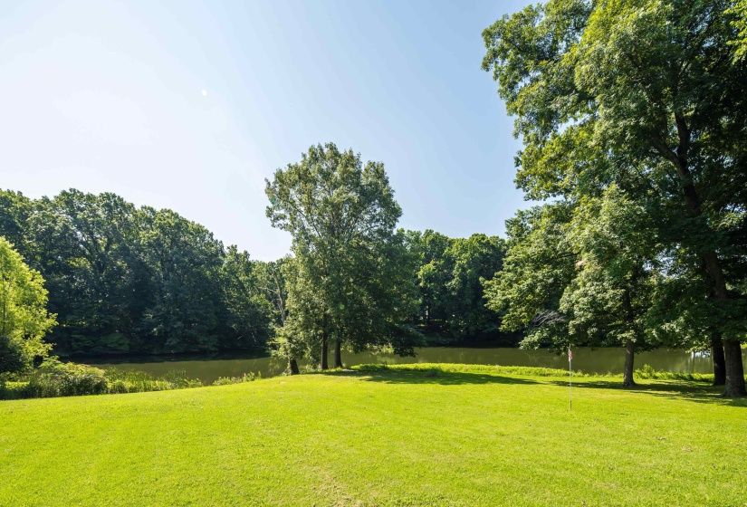 Expansive grassy lawn bordered by mature trees and a tranquil body of water