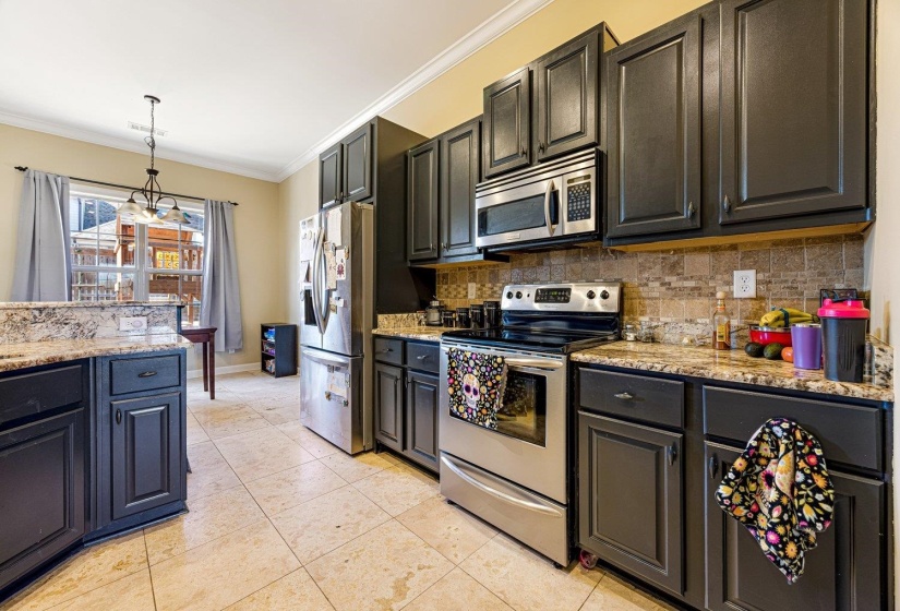 Kitchen featuring dark cabinetry, lighter granite countertops, a tiled backsplash, and stainless steel appliances