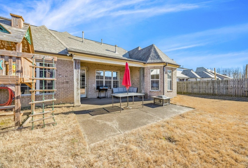 Spacious backyard featuring a concrete patio, covered porch area, and brick exterior with multiple windows