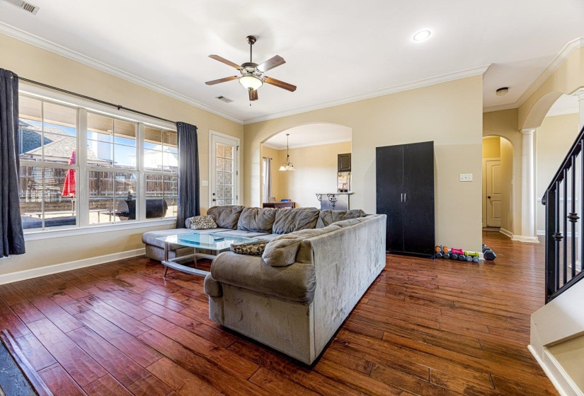 Spacious living area featuring wood-finish flooring, a ceiling fan, and large windows with transom details