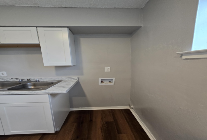 Laundry area with dark wood-type flooring, a textured ceiling, washer hookup, and cabinet space