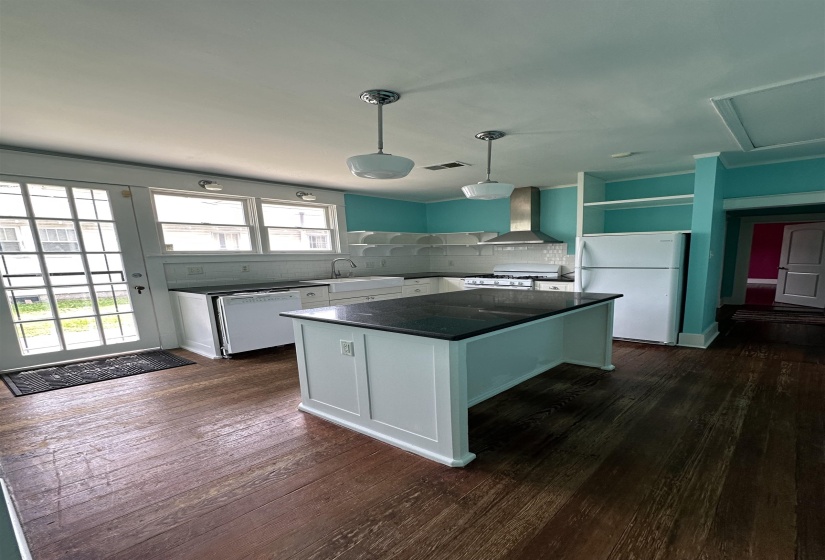 Kitchen featuring dark wood-finish flooring, white cabinetry, a central island with a dark countertop, subway tile backsplash, and a stainless steel range hood