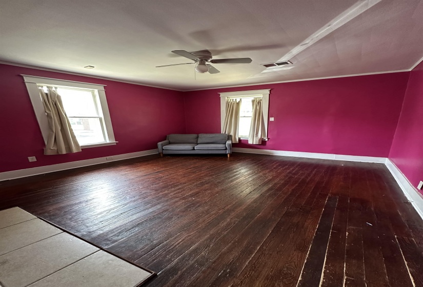 Spacious room featuring dark wood-finish flooring, two windows with white trim, a ceiling fan with light fixture, and a white baseboard
