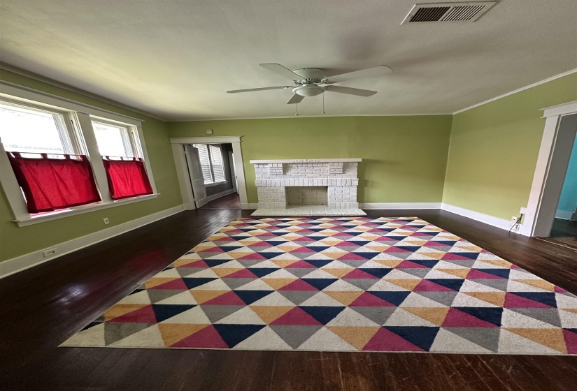Living area featuring dark wood-finish flooring, a white brick fireplace, multiple windows with white trim, and a ceiling fan