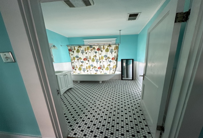Bathroom featuring a clawfoot tub, white beadboard wainscoting, and black and white hexagonal tile flooring